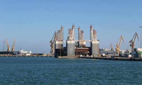 View of Cádiz industrial port with cranes and oil rig on a sunny day.