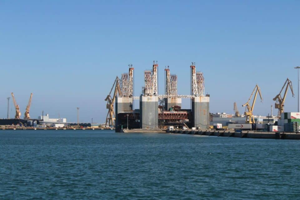 View of Cádiz industrial port with cranes and oil rig on a sunny day.