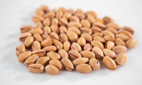 A close-up view of scattered pistachios on a white background, emphasizing texture.