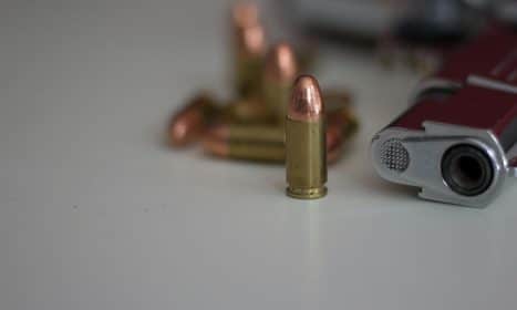 A detailed image of a handgun and multiple bullets on a white background, showing focus on firearm elements.