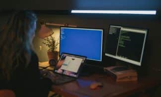 Woman using multiple screens for cybersecurity tasks in a cozy home office