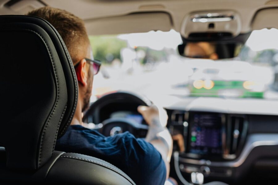 Close-up of a man driving a modern vehicle from behind with a blurred urban background.