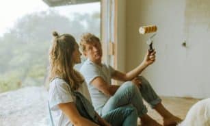 A young couple sits indoors planning their home renovation with a paint roller.