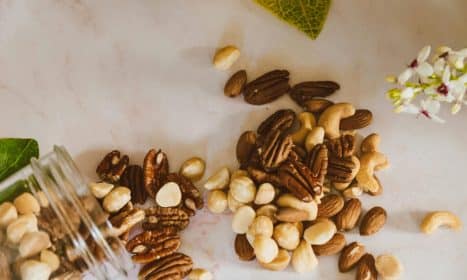 A close-up of mixed nuts spilled from a jar, featuring pecans, cashews, and almonds on a marble surface.