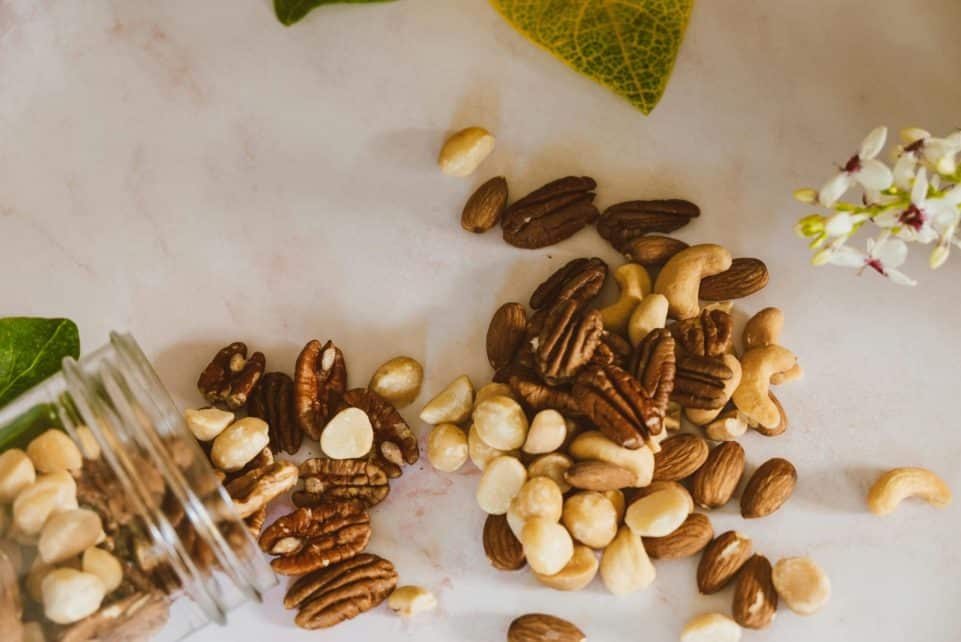 A close-up of mixed nuts spilled from a jar, featuring pecans, cashews, and almonds on a marble surface.