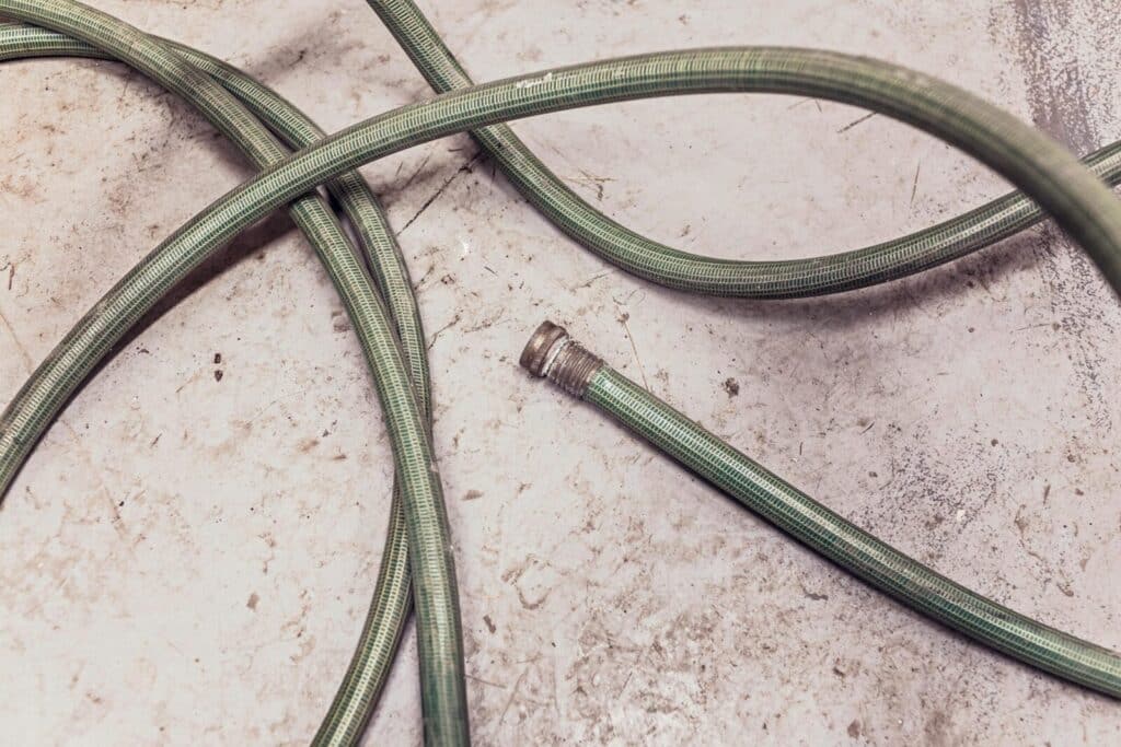 A green garden hose coiled and lying on a textured concrete surface.