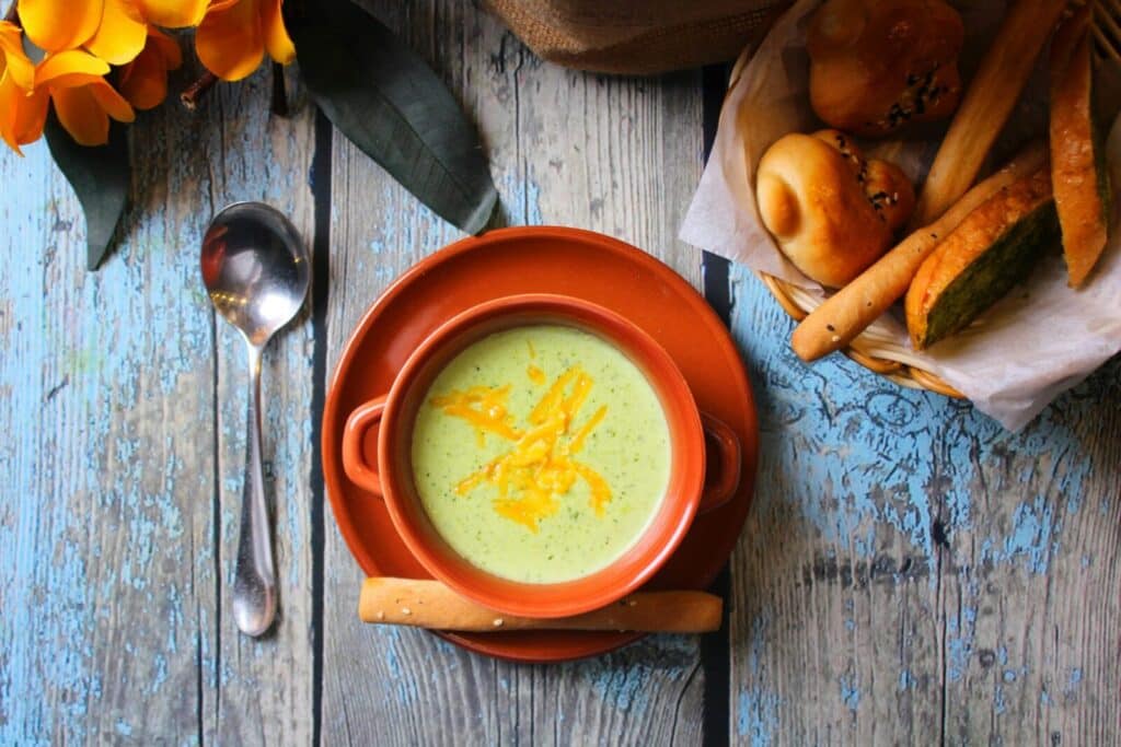 Top view of a delicious green vegetable soup with bread basket on a rustic wood table setting.