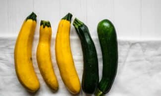 A variety of fresh zucchini and yellow squash on a white cloth background, ideal for healthy cooking.