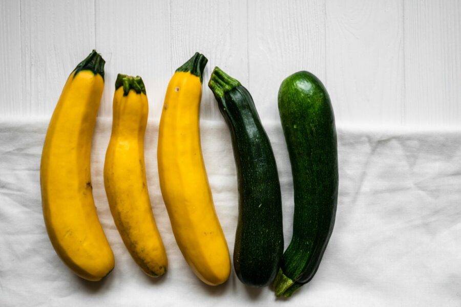 A variety of fresh zucchini and yellow squash on a white cloth background, ideal for healthy cooking.