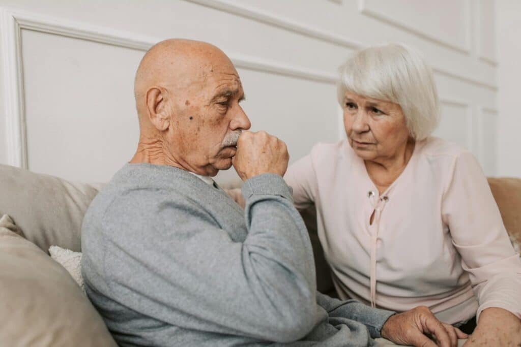 An elderly couple sitting on a couch, showing care and affection indoors.