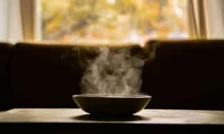 A steaming bowl of soup on a wooden table indoors with soft autumn light through a window.