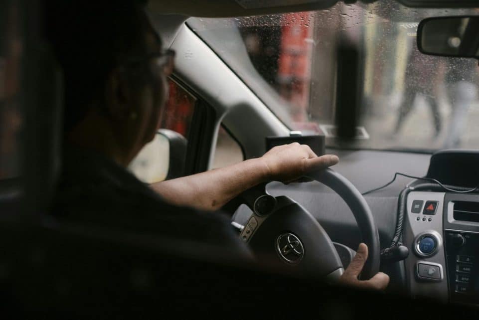 Back view of crop anonymous man in eyeglasses driving car in rainy day