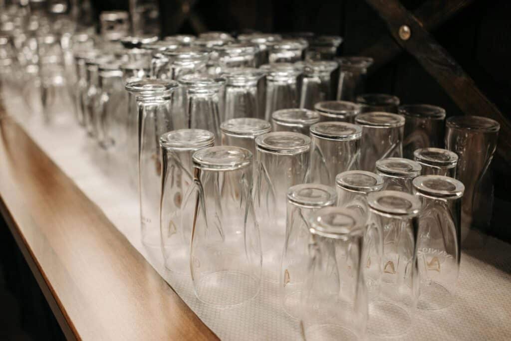 A neat arrangement of upside down drinking glasses on a wooden shelf in a dimly lit setting.
