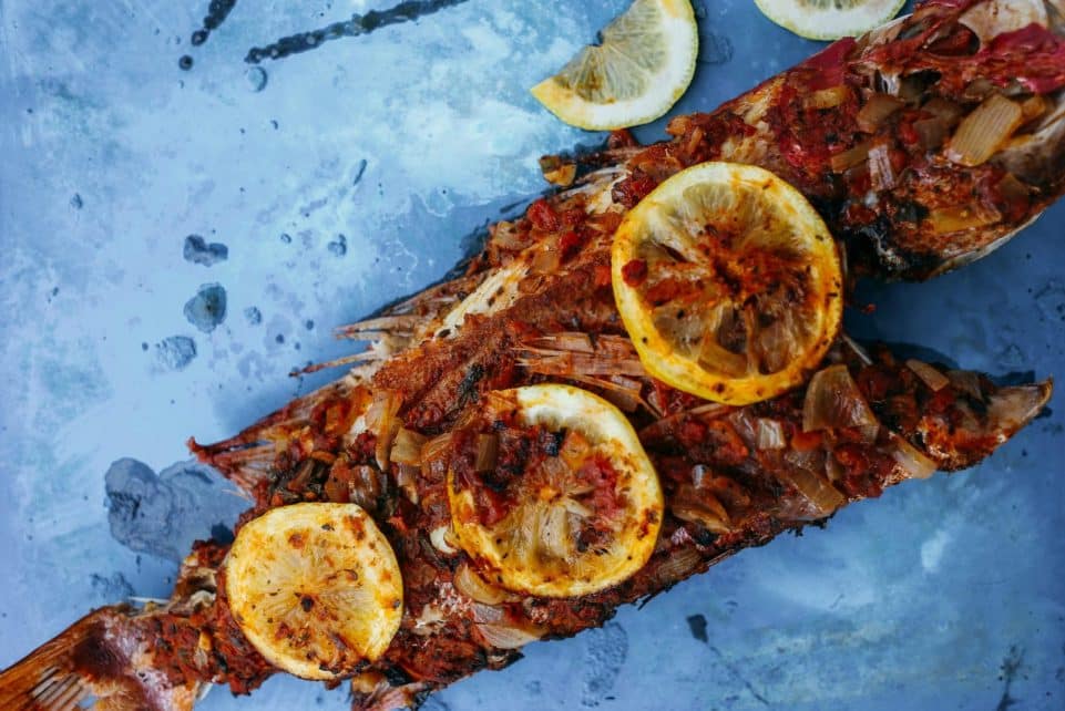 Deliciously grilled fish topped with lemon slices on a textured blue surface.