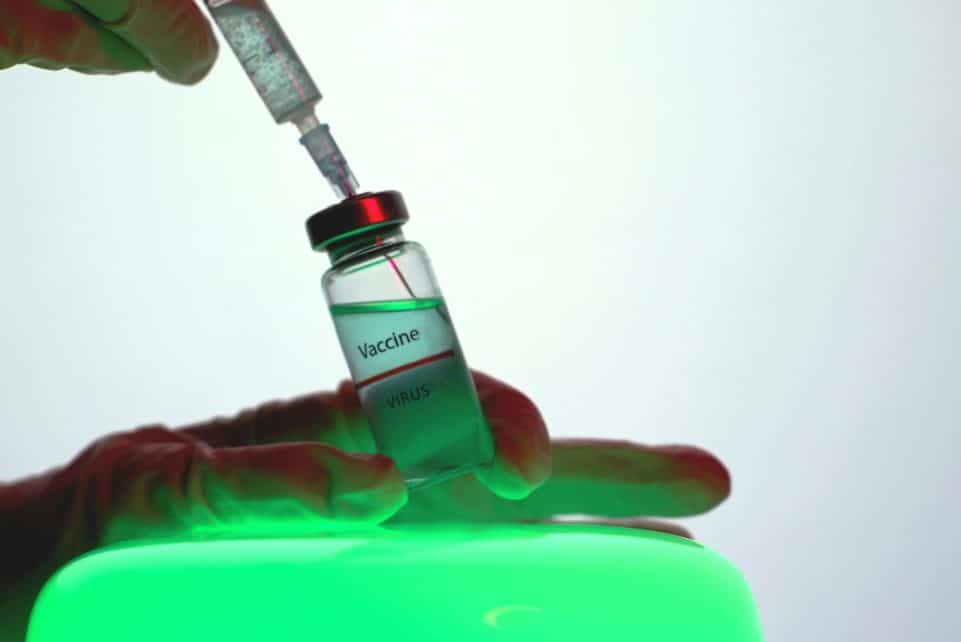 Syringe drawing vaccine from vial, symbolizing immunization efforts.
