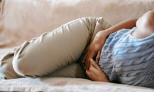 Crop faceless female in casual wear lying on sofa while having acute pain in stomach