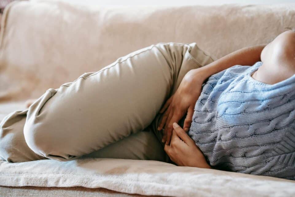 Crop faceless female in casual wear lying on sofa while having acute pain in stomach
