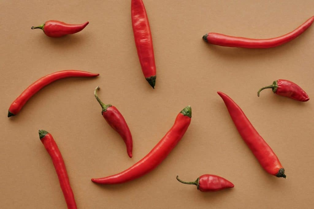 Flat lay of red chili peppers arranged on a brown textured background, showcasing vibrant color contrast.