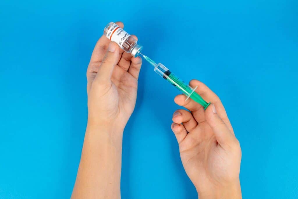 Hands holding a syringe and COVID-19 vaccine vial on a blue background.