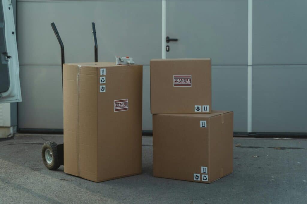 Three cardboard boxes on a dolly, ready for shipping outside a warehouse.