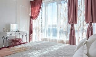 Bright, elegant bedroom with chic decor, featuring pink drapes and a comfortable bed, exuding luxury and style.