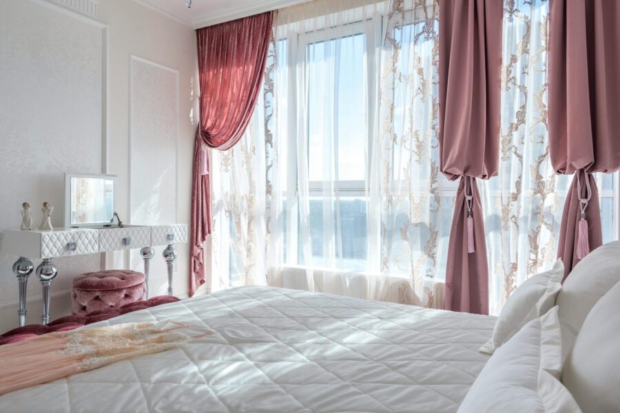 Bright, elegant bedroom with chic decor, featuring pink drapes and a comfortable bed, exuding luxury and style.