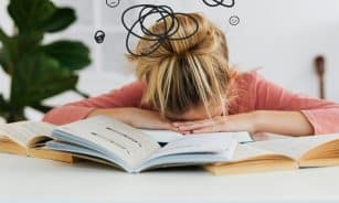 Young woman asleep over books at desk, conveying stress and mental overload.