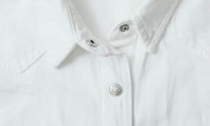 Detailed view of a white shirt with metal buttons and textured fabric.