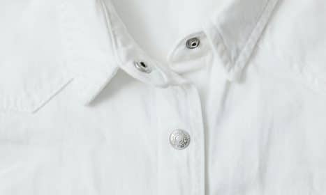 Detailed view of a white shirt with metal buttons and textured fabric.