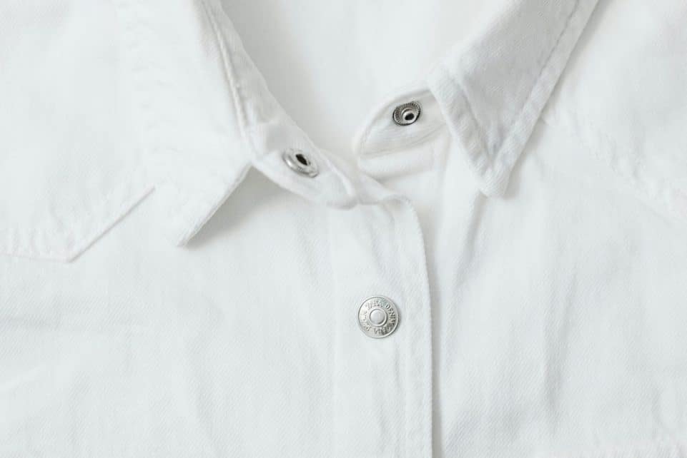 Detailed view of a white shirt with metal buttons and textured fabric.