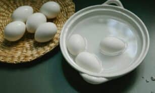 Boiled and raw white eggs arranged in a ceramic bowl and wicker tray on a kitchen surface.