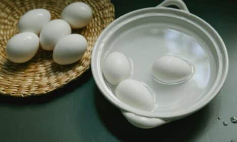 Boiled and raw white eggs arranged in a ceramic bowl and wicker tray on a kitchen surface.