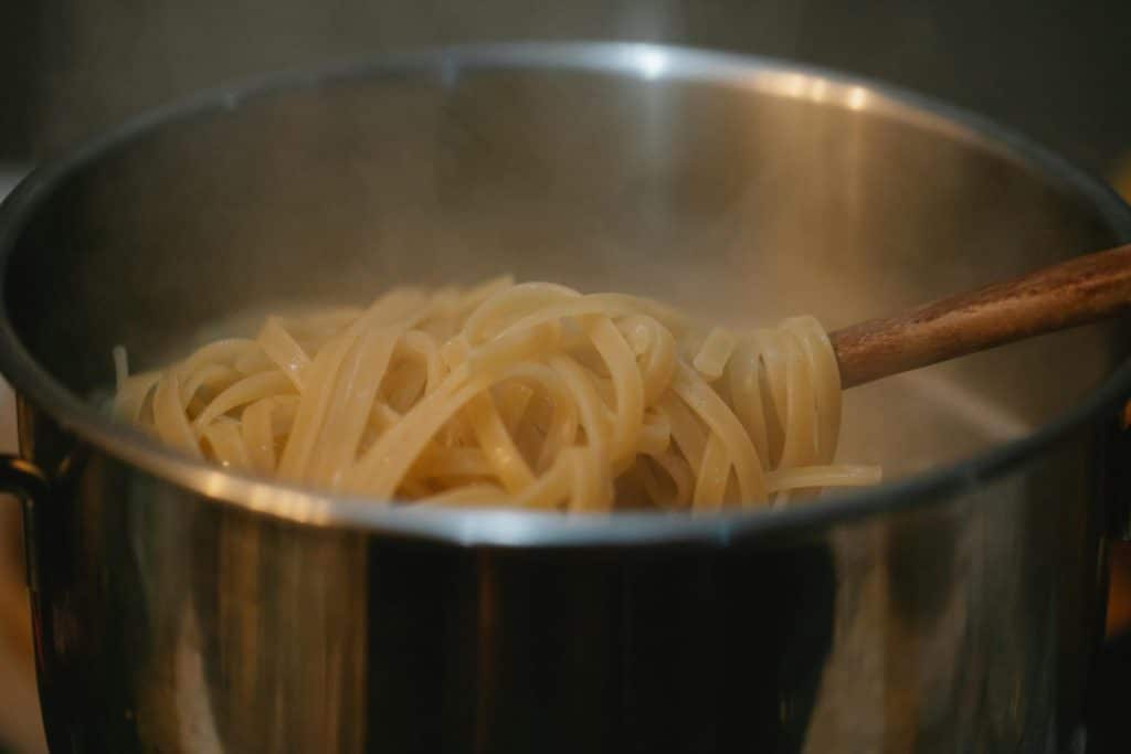 Close-up of steaming spaghetti cooking in a stainless steel pot with wooden utensil.
