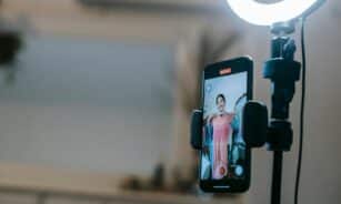 A woman livestreaming with a smartphone and ring light in a modern home setting.