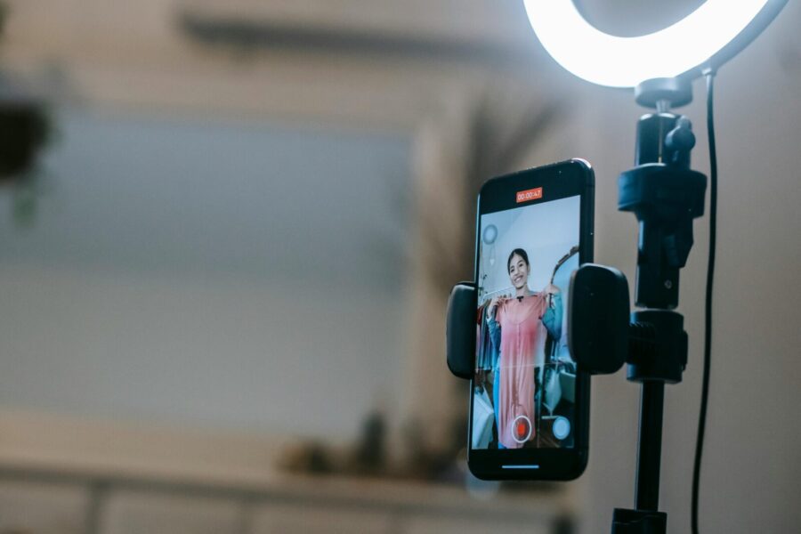 A woman livestreaming with a smartphone and ring light in a modern home setting.