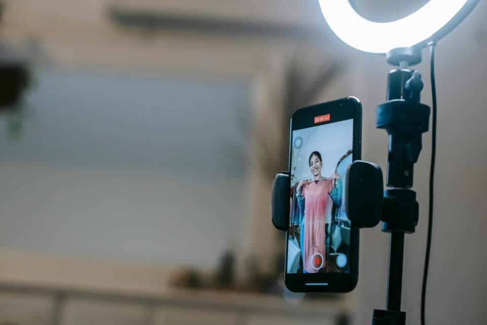 A woman livestreaming with a smartphone and ring light in a modern home setting.