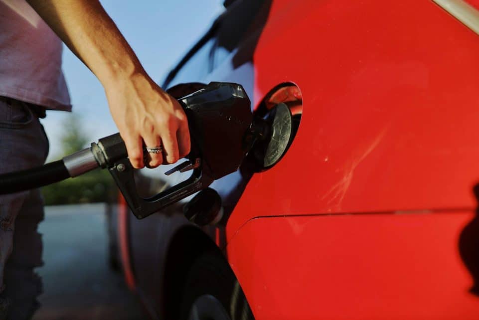 Close-up of a person refueling a red car at an outdoor gas station during the day.