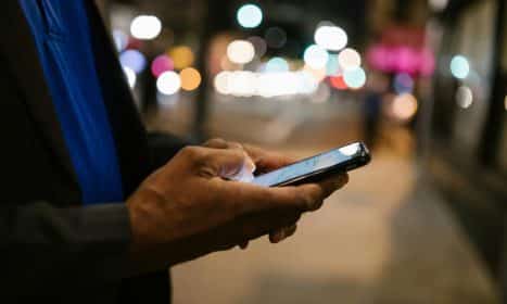 Close-up of a man using a smartphone on a busy city street at night.