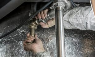 Close-up of a plumber's hands installing steel pipes indoors, showcasing skilled manual work.