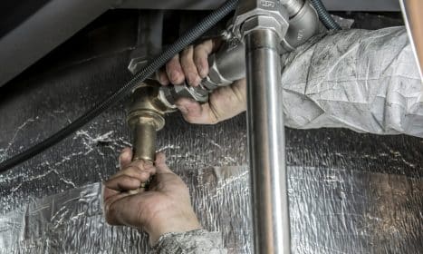 Close-up of a plumber's hands installing steel pipes indoors, showcasing skilled manual work.