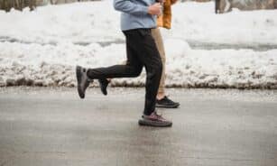Two individuals jogging on a snow-lined roadway, showcasing winter fitness and outdoor activity.
