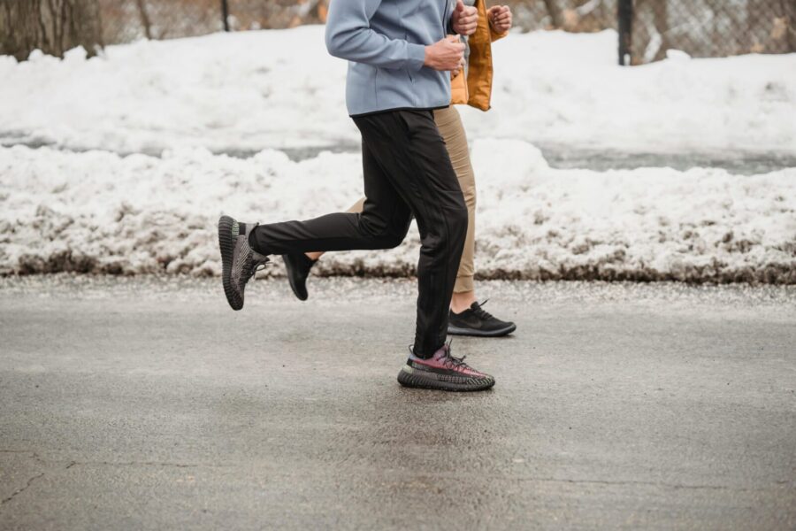Two individuals jogging on a snow-lined roadway, showcasing winter fitness and outdoor activity.