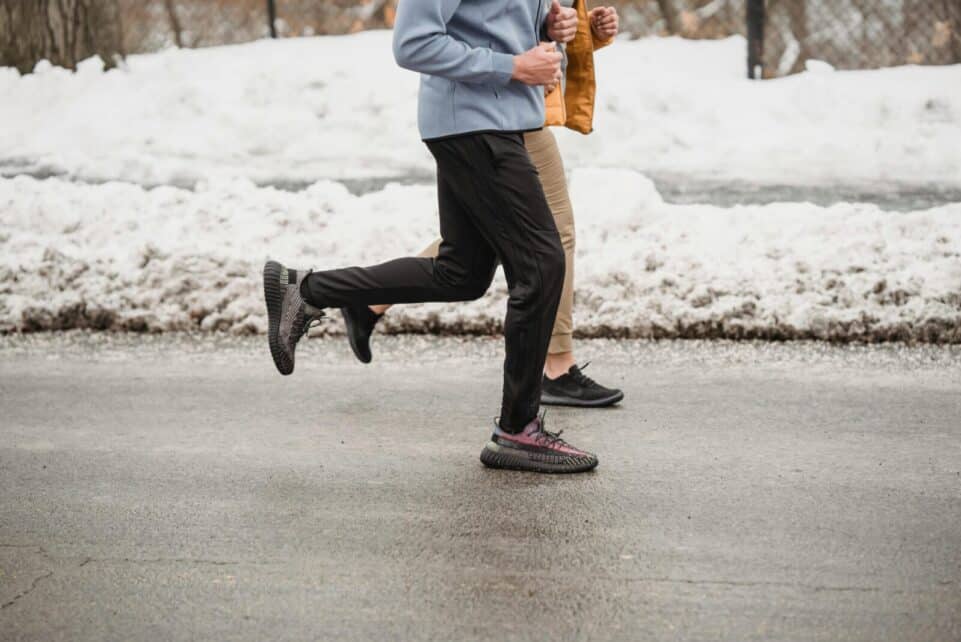 Two individuals jogging on a snow-lined roadway, showcasing winter fitness and outdoor activity.