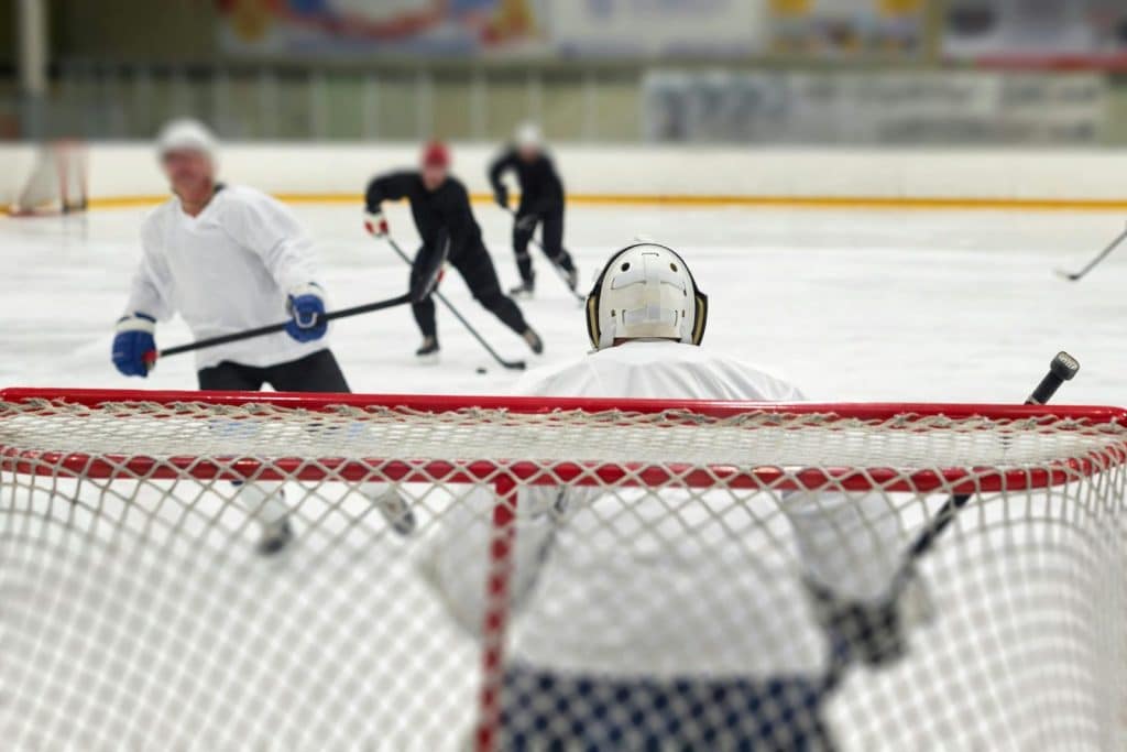 An intense ice hockey game featuring a focused goalie ready to defend the net against advancing players.
