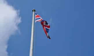 Union Jack flag waving on a flagpole against a clear blue sky in London, UK.