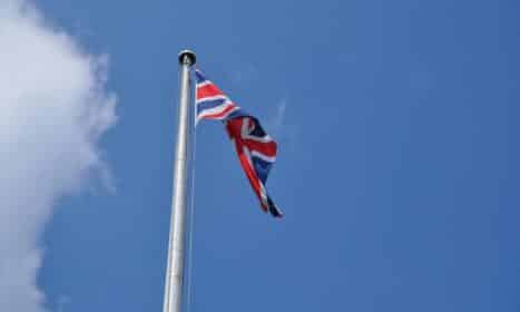Union Jack flag waving on a flagpole against a clear blue sky in London, UK.