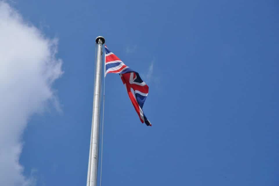 Union Jack flag waving on a flagpole against a clear blue sky in London, UK.
