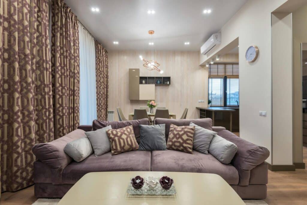 Soft comfortable couch with various cushions and coffee table placed in cozy living room with dining zone