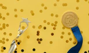 Golden medal and silver trophy with confetti on yellow surface, celebrating achievement.