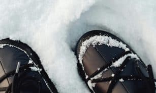 Close-up view of black winter boots covered in fresh snow.